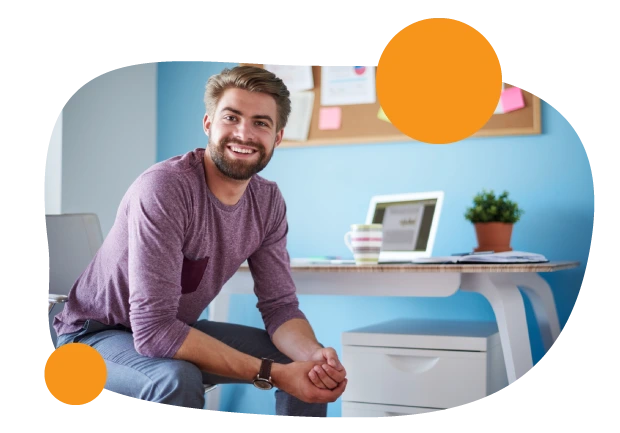 Hombre sonriendo trabajando desde casa, de fondo se ve la laptop y una taza de café